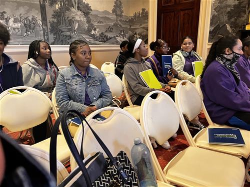 Students sitting on fold-up chairs in a conference room.